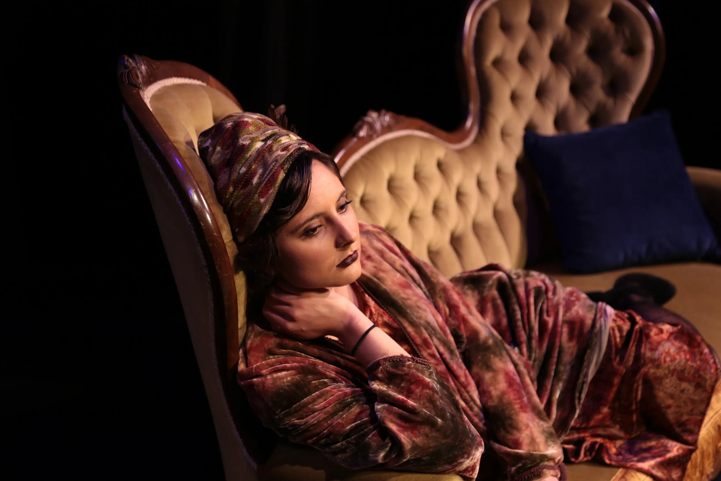 A reclining figure dressed in richly patterned textiles on an ornate chair